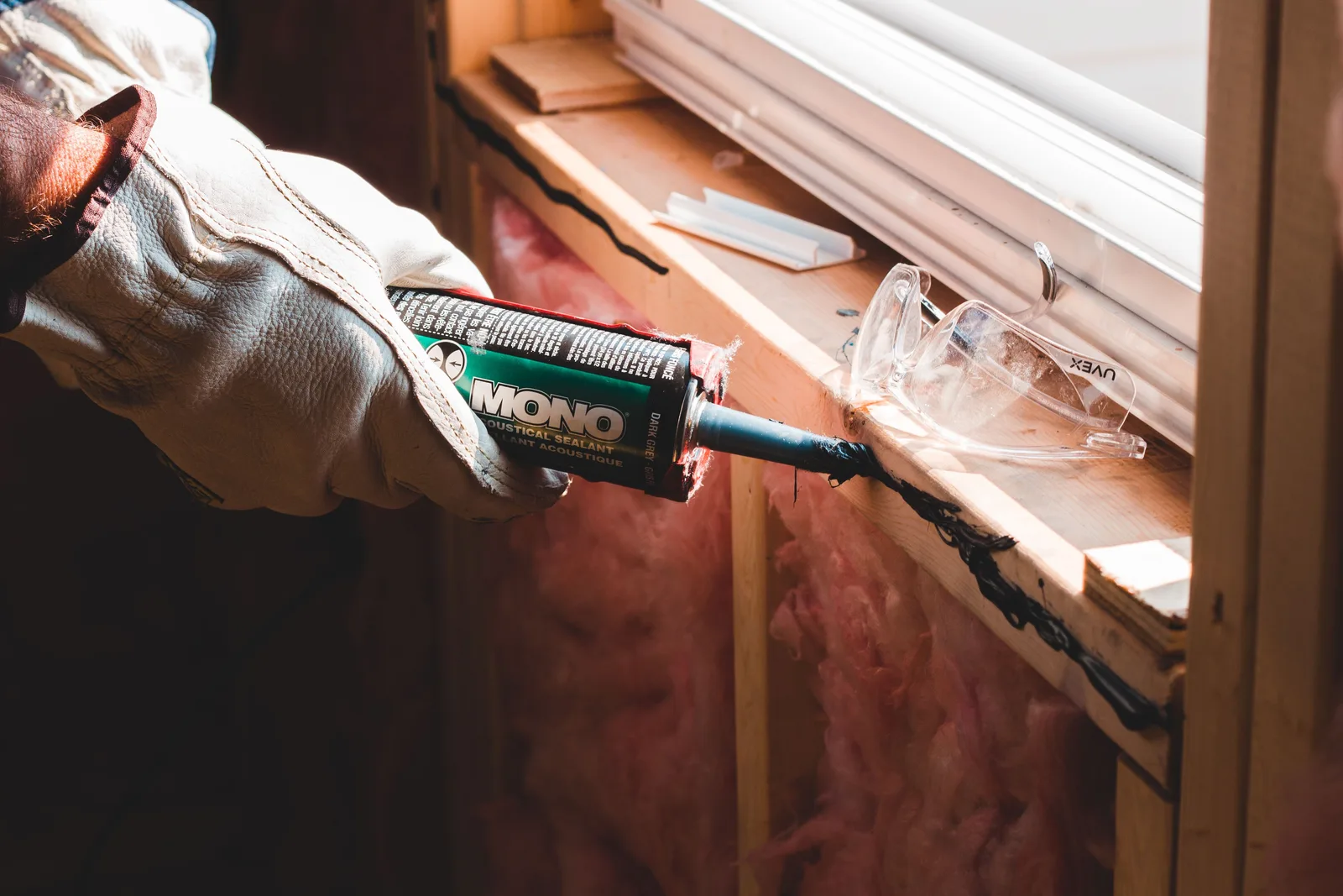 Crop unrecognizable workman in glove applying caulk from bottle on seam during window montage work in building. A small room's first year maintenance calendar, from month one to detector checks