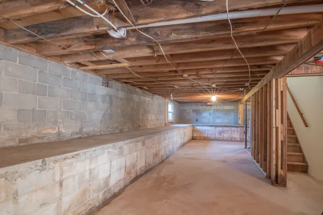 Empty basement with exposed wooden beams, concrete walls and stairs. What Are Calgary Secondary Suite Requirements for Small Basements?