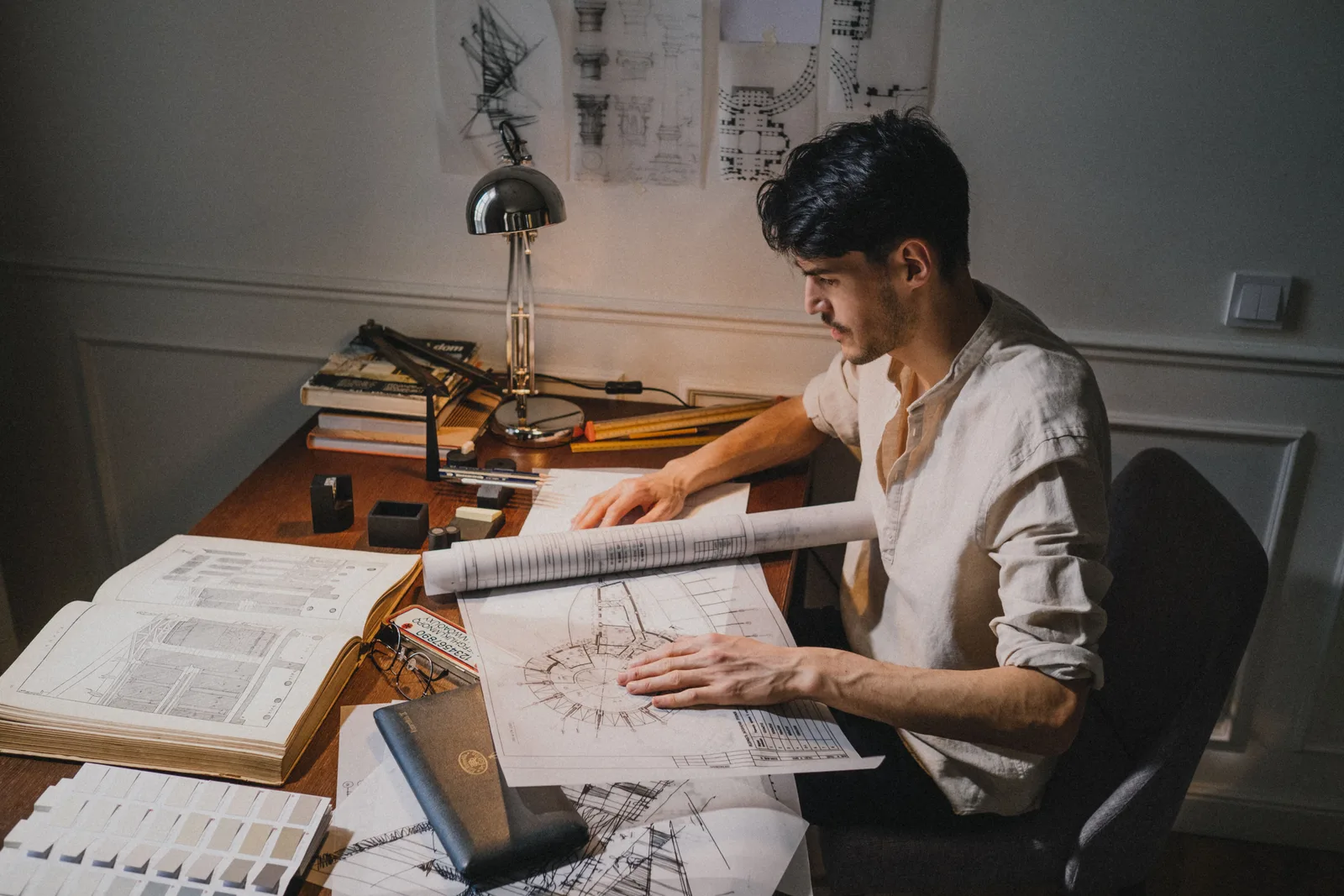 Young architect at a desk working on blueprint designs under lamp light. Recurring small home design firm problems, and the guide to fixing each