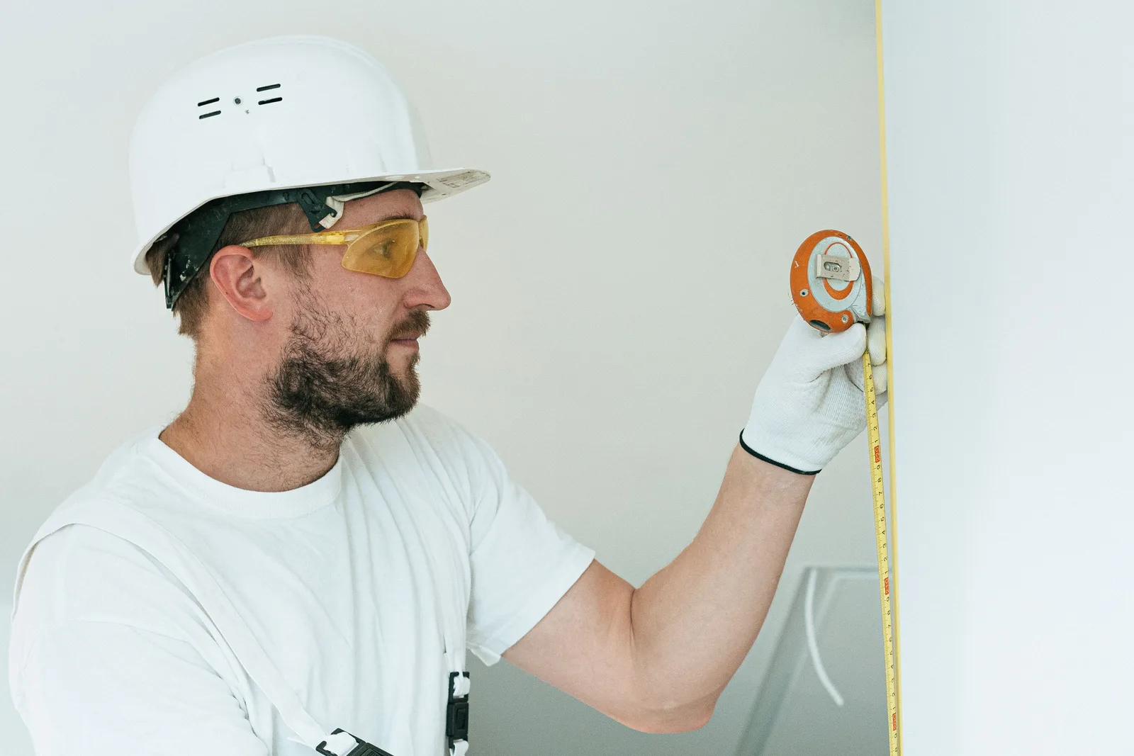 Construction worker with hard hat and goggles measuring a wall with a tape measure. Preventing small space design mistakes: tools to test and two alarms