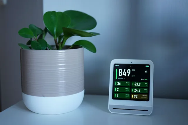 Air quality monitor next to a potted plant on a desk, showing CO2 and PM2.5 levels. Wildfire smoke filtration in a Kelowna or Calgary small home, what to retrofit